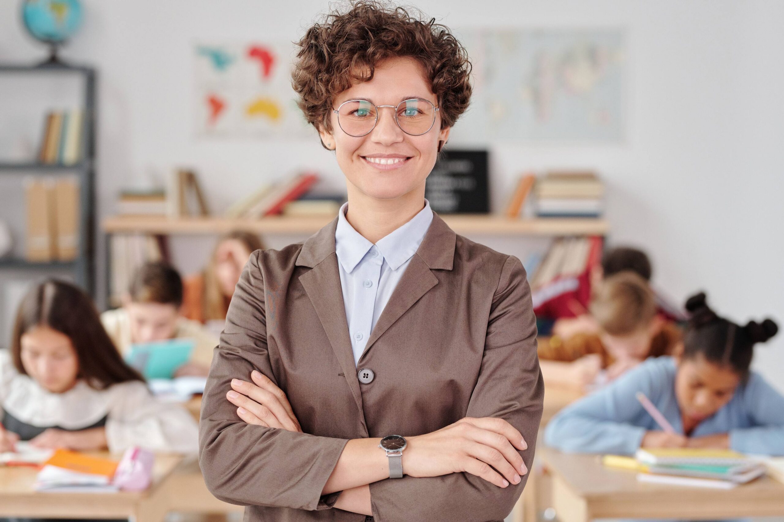 Smiling teacher standing confidently in a classroom with students working in the background